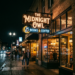 Neon sign for The Midnight Owl Books & Coffee on a city street at night with people walking by and illuminated storefront.